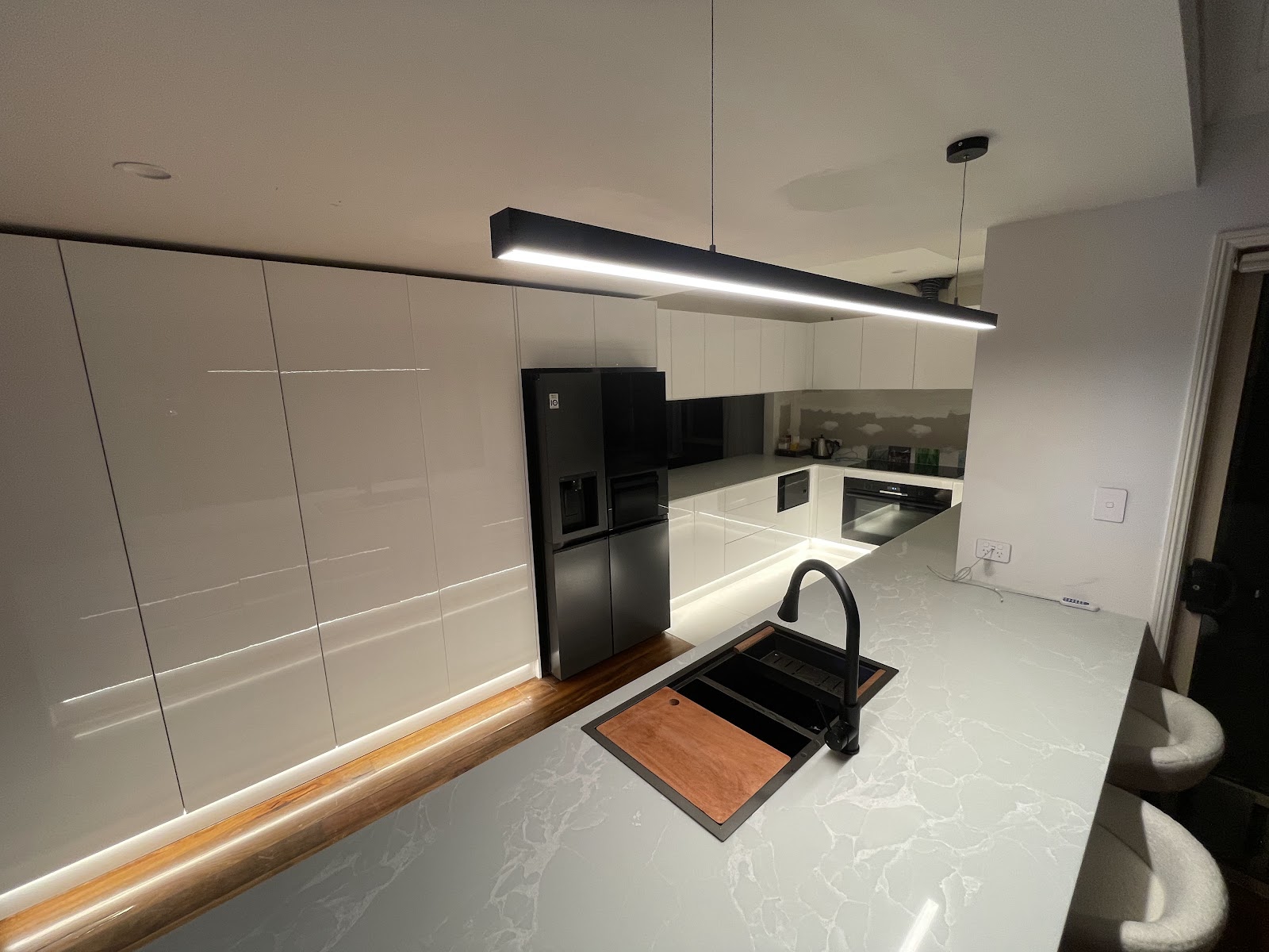 Kitchen at night lit by a black linear LED pendant over a stone island and LED strip under the cabinets