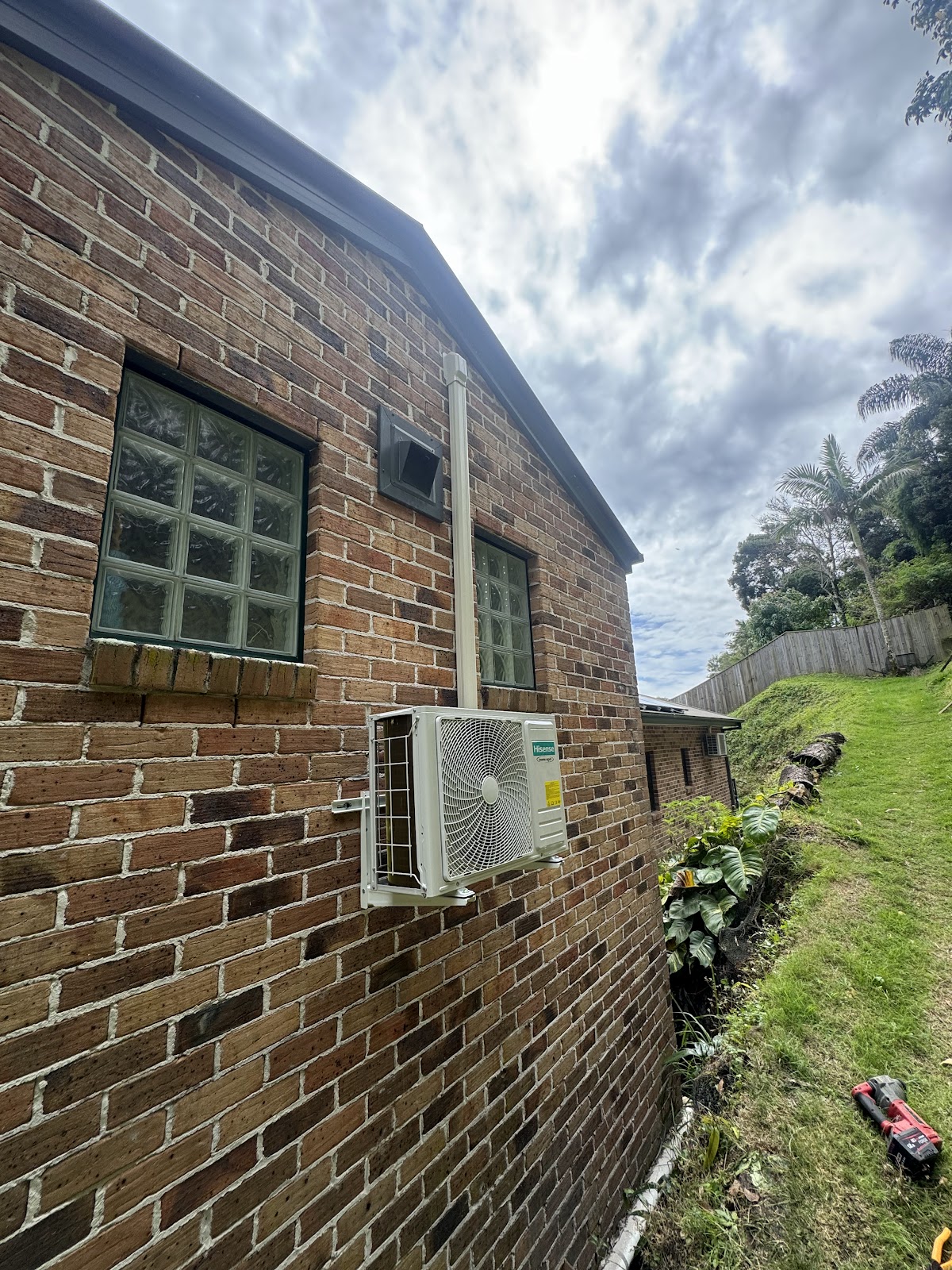 Split system outdoor unit on the side of a brick house with palms behind